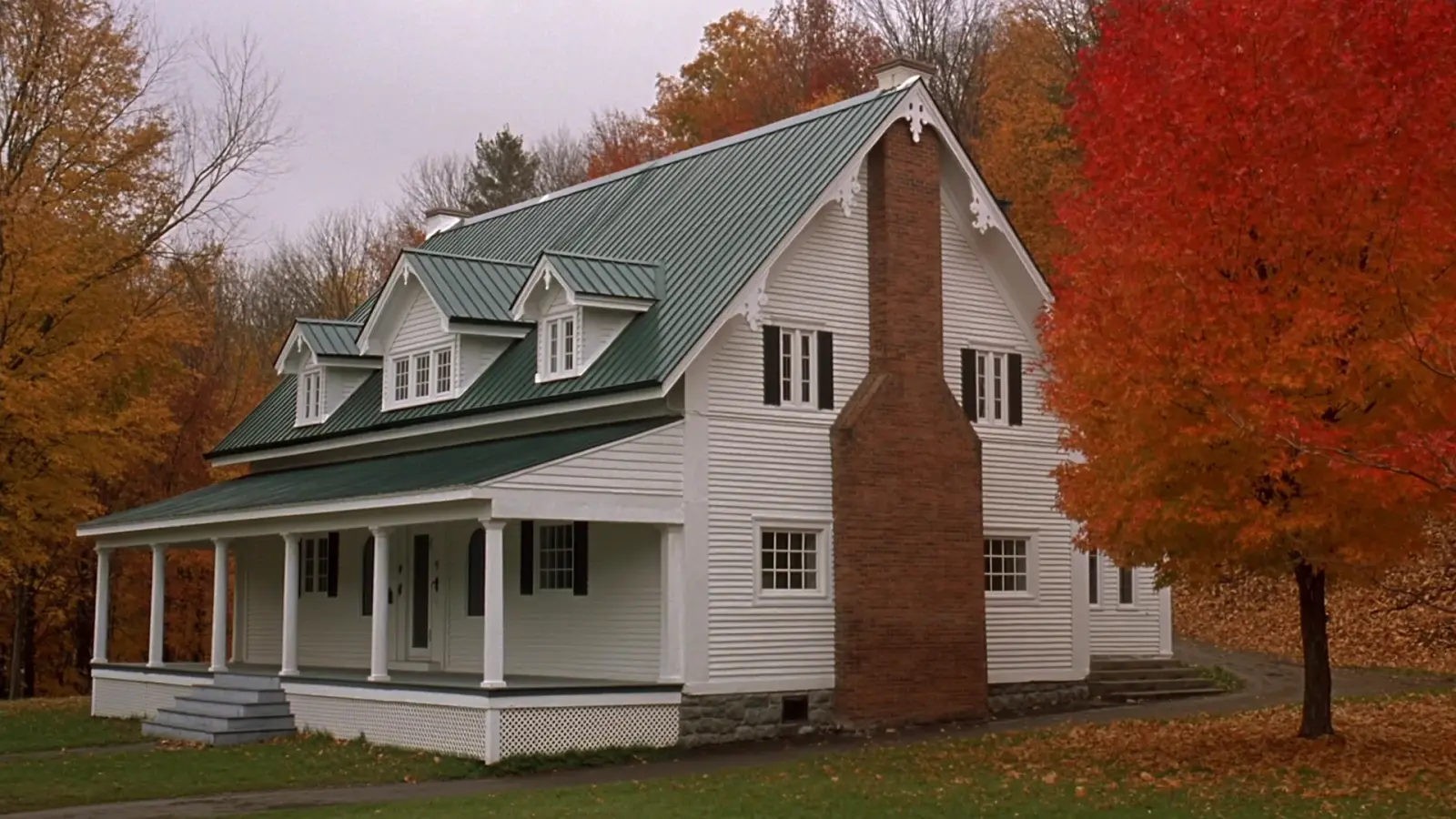 Historic white Vermont farmhouse with decorative gable trim and a dark green standing seam metal roof among autumn maples