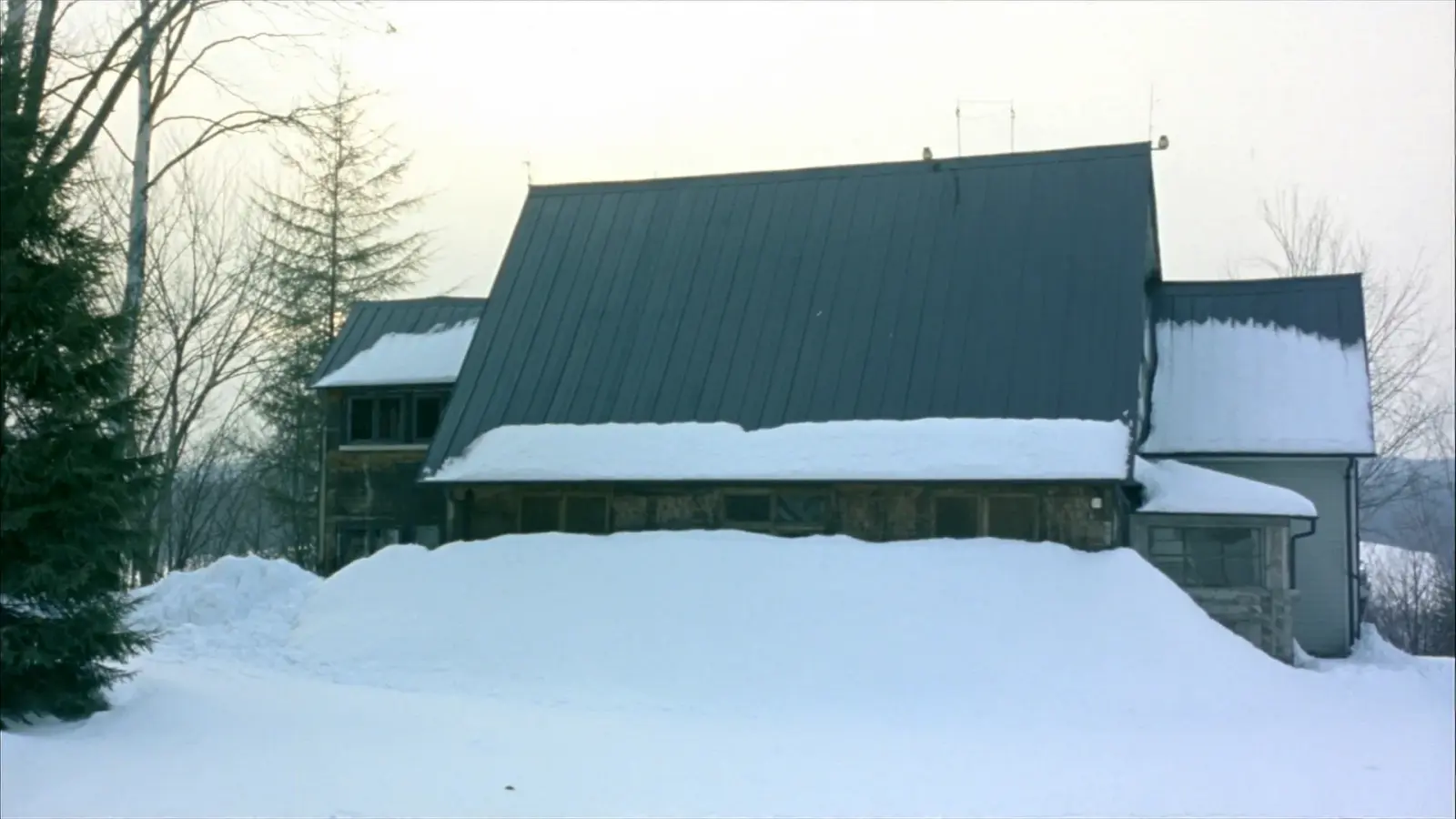 Snow shed from a standing seam metal roof piled in a deep bank along the eaves of a Vermont home in winter